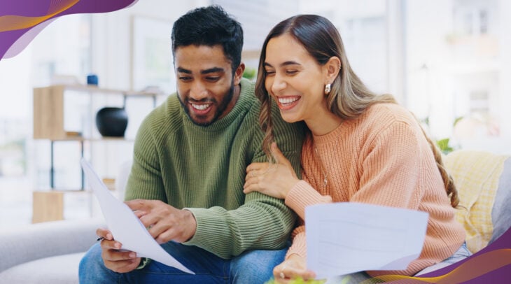 Man and woman couple sitting on couch at home looking at paperwork together.