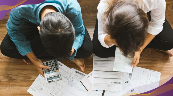 Couple sitting on wood floor looking down going over financial paperwork.