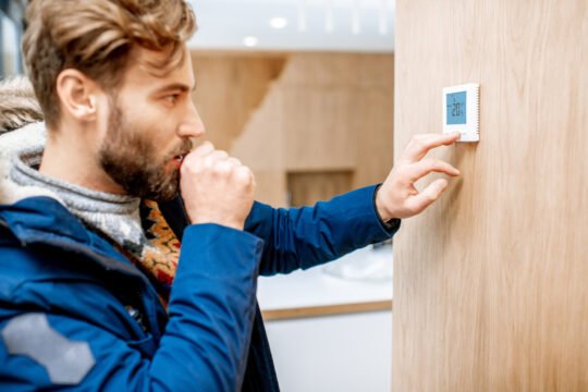 Man adjusting temperature with thermostat at home