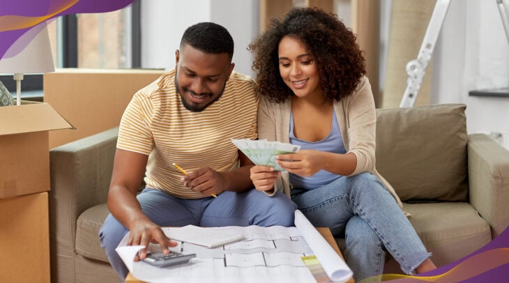 Man and woman couple sitting on couch looking at home plans and using calculator.