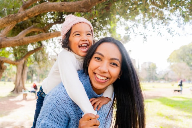A mom holds her child on her back.
