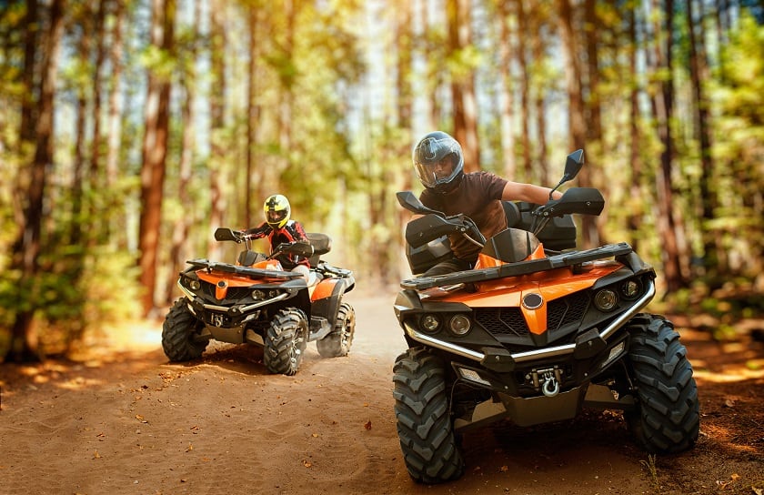 A pair of ATV riders drive on desert trail in woods