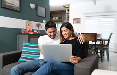 Young happy couple share laptop while sitting on couch