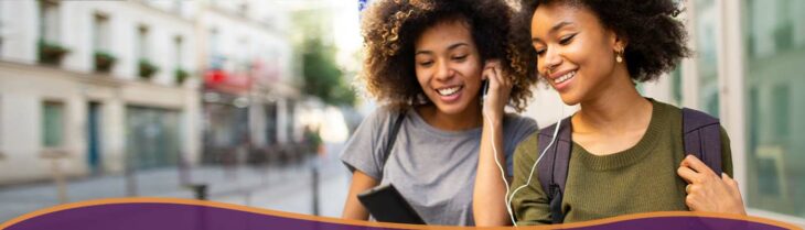 Two friends smiling taking a walk looking at phone together.