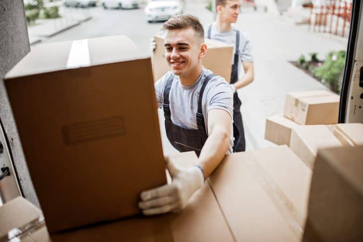 Two young men carry boxes from back of truck