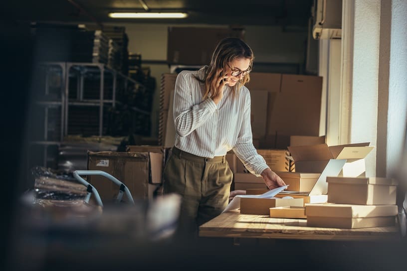 Business woman on phone looks at documents in warehouse