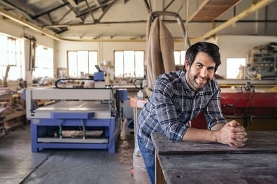 Smiling man stands near woodworking equipment inside woodshed