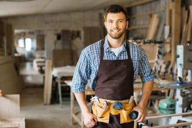 Young male carpenter with toolbelt inside wood shed