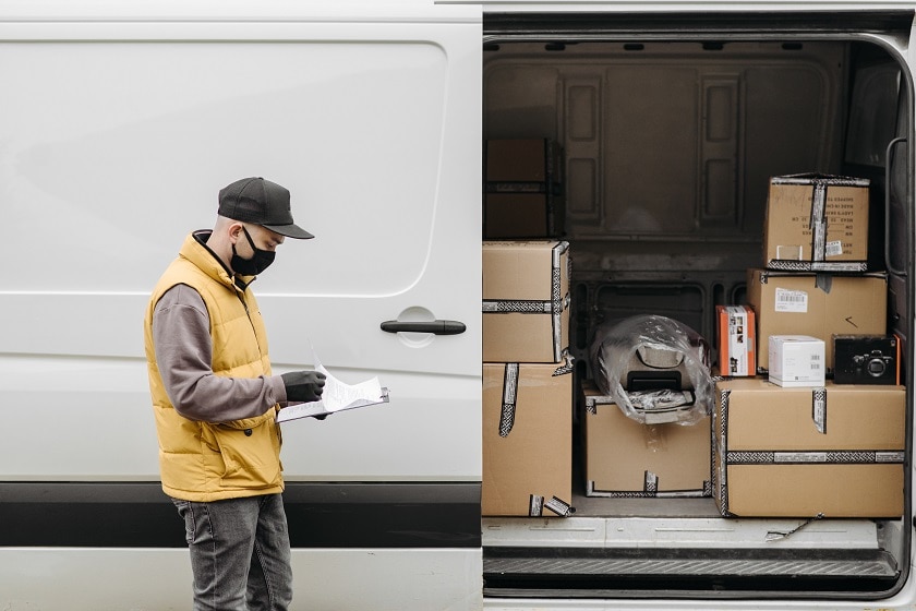 A worker checks his clipboard next to his van that is full of packages waiting for delivery