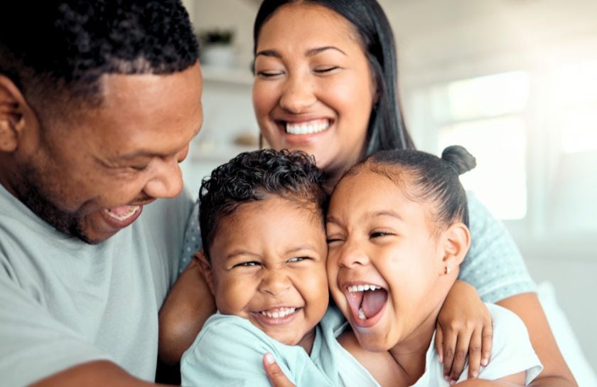 A mom and dad embrace their two young children, with very happy faces.