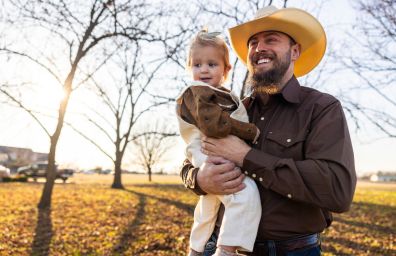 A rancher holds his daughter in the sun.