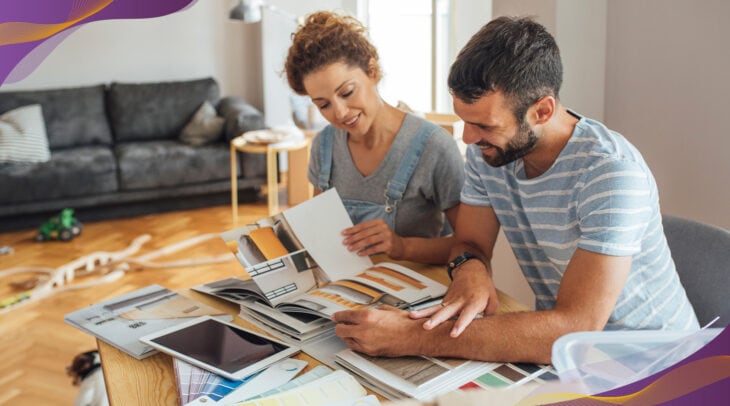 Happy couple looking at design books and materials options at kitchen table.