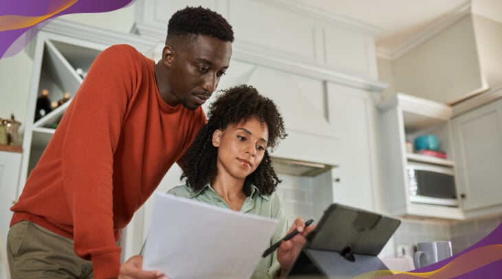 Man and woman at home in kitchen looking at documents and tablet together.