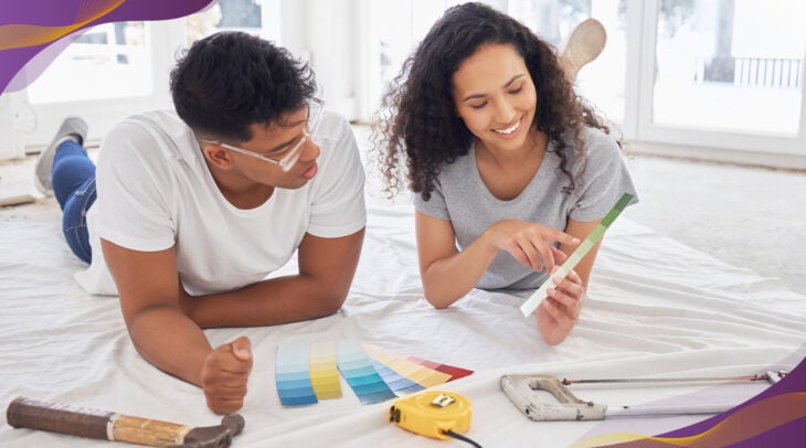 Young couple laying on floor of living room looking at paint samples together.