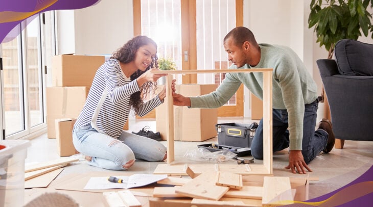Young couple building furniture shelves together in living room.
