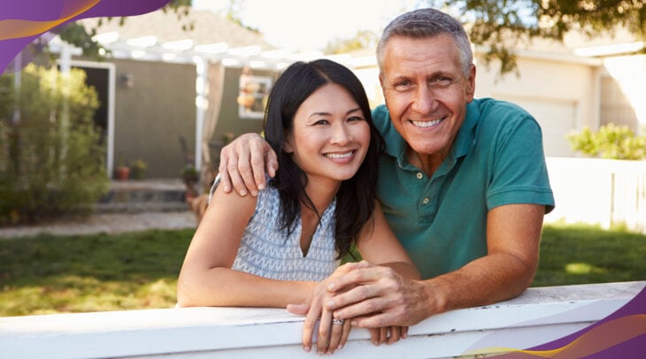 Happy couple standing outside their home in yard smiling.