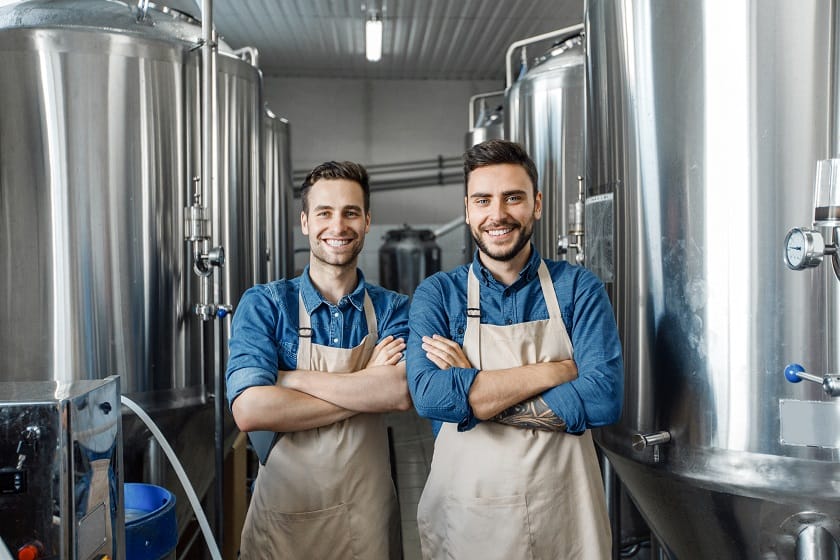Two male coworkers at factory post with large dairy storage equipment