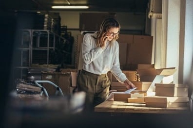 A female business owner uses cell phone and laptop to perform transaction