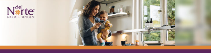 New mom holding baby in kitchen smiling looking at smartphone