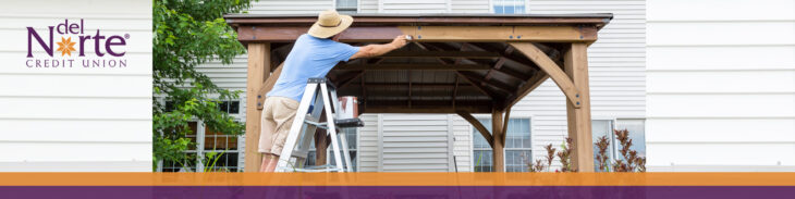 Man painting outdoor deck covering standing on ladder.