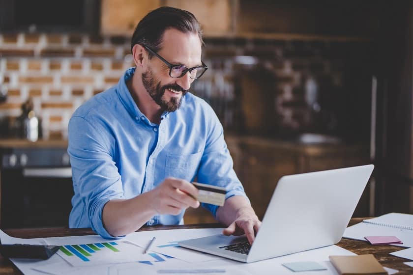 Business Owner Using Credit Card And Laptop Computer In Kitchen