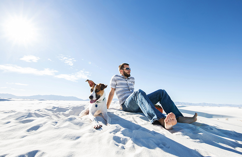 Man and dog sit on sand at White Sands National Park in New Mexico