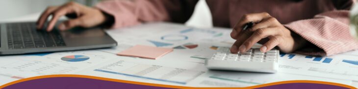 Woman looking over graphs and documents on laptop with calculator.