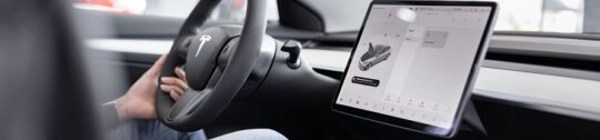 A driver with one hand on the steering wheel of an electric vehicle