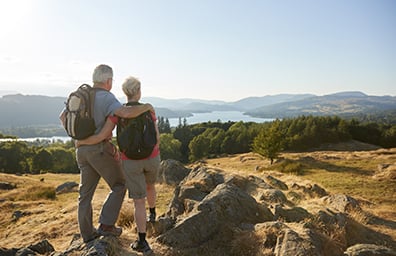 Senior couple with small backpacks walk trail with view of lake