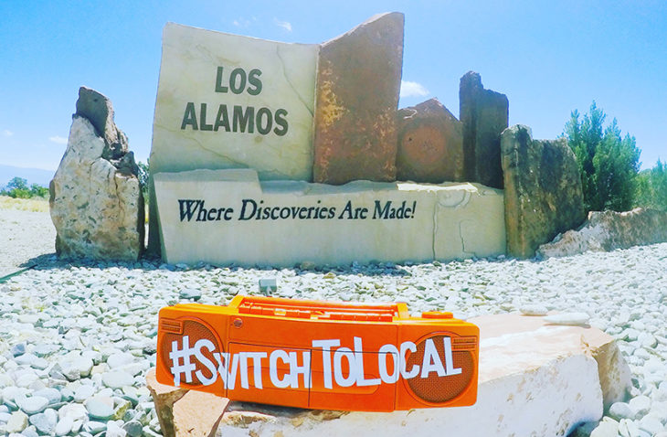 Los Alamos welcome sign that reads "Where discoveries are made!" with switch to local hashtag in forefront