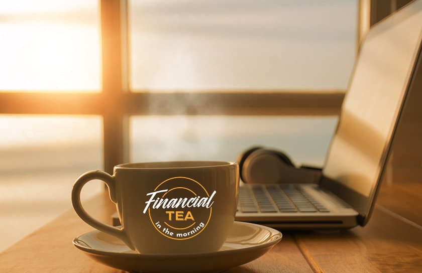 A cup of tea with Financial Tea In The Morning logo next to laptop at dawn