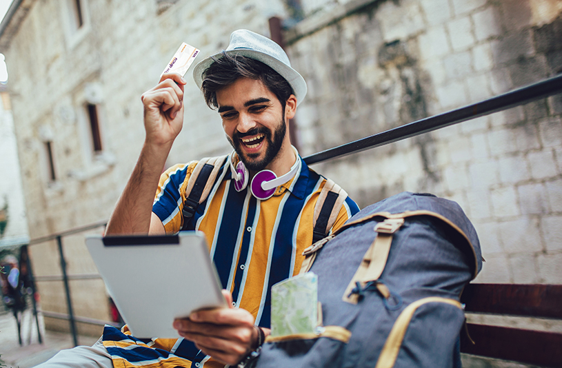 Happy Hispanic male traveler holds credit card in one hand and tablet in other hand