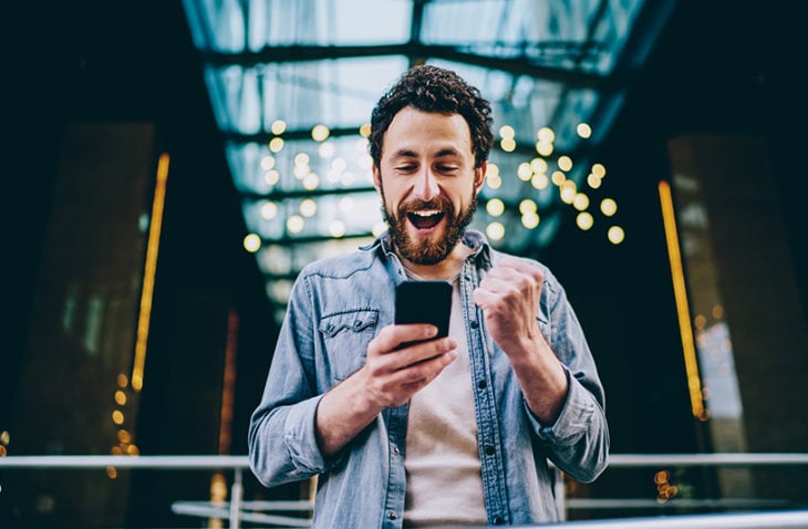 Happy man looks at cell phone and clenches fist