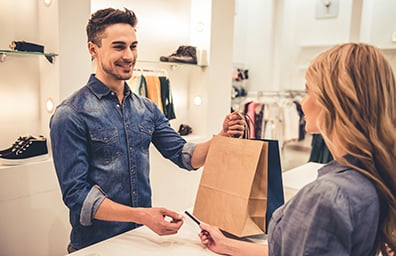 Smiling man working retail hands bag to female customer