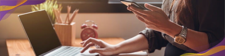 Person working at laptop holding smartphone.