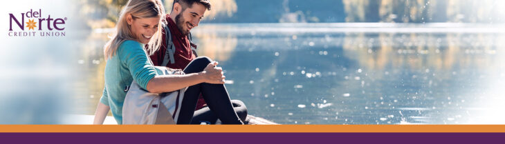 Man and woman on a date at a lake sitting on the dock in the sunshine laughing.