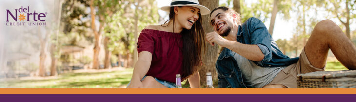 Man and woman on a date in the park having a picnic, smiling and laughing, picnic basket on blanket.