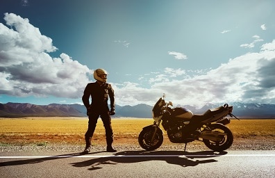 Man with helmet on stands next to motorcycle in desert