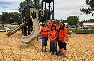Four DNCU employees stand next to children's slide in Espanola New Mexico