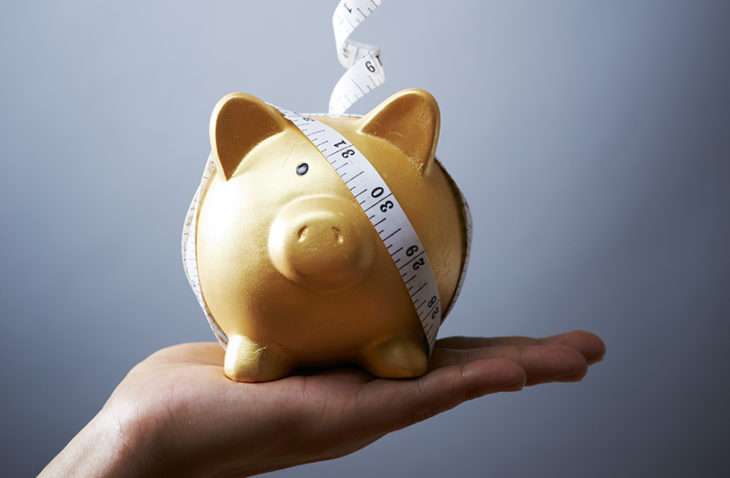 Piggy bank wrapped in measuring tape held up by human hand