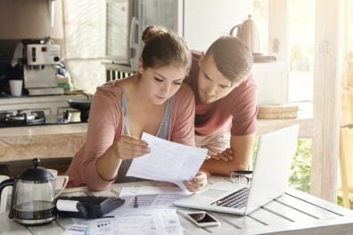 Young couple in kitchen considers financial documents near laptop