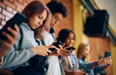 Teenagers in a line, checking their mobile phones.