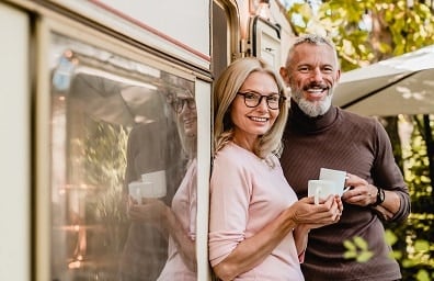 Middle aged couple smile and drink coffee just outside of RV