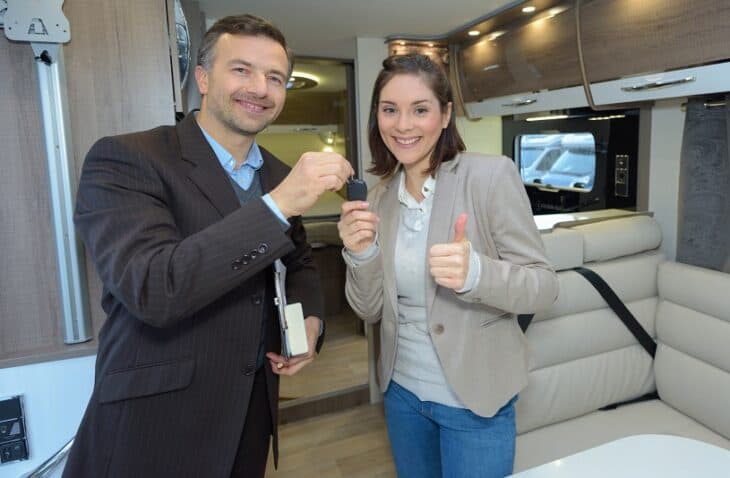 Salesman hands keys to happy female customer inside RV