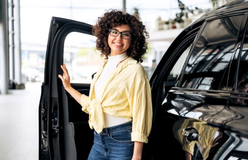 A lovely lady stands next to a new black car.