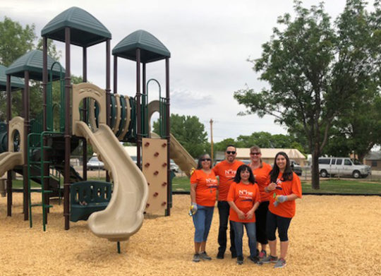 Four DNCU employees stand next to children's slide in Espanola New Mexico
