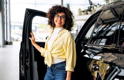 A young woman stands next to her new purchase, a black SUV.