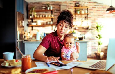 A woman holds her baby, while she works on bills.