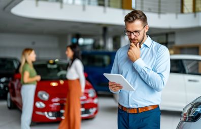 A man contemplates while looking at his tablet in a car showrrom.