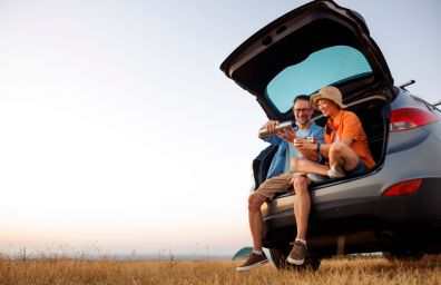 A couple enjoy a warm beverage on a cool morning, in the back of their car.